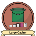 A stylized metalic badge. It appears to be made of bronze and features a colored bucket-type container with symbols for the different cache sizes underneath – the one for large caches is colored in. A ribbon reading Large Cacher sits on the bottom.